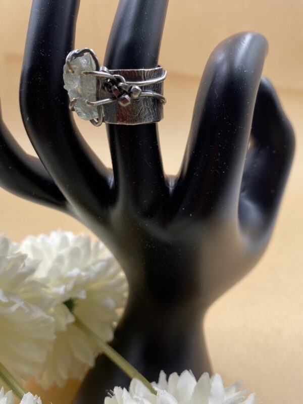 Sterling silver ring with prongs holding a raw aquamarine stone with antique Indian dangle