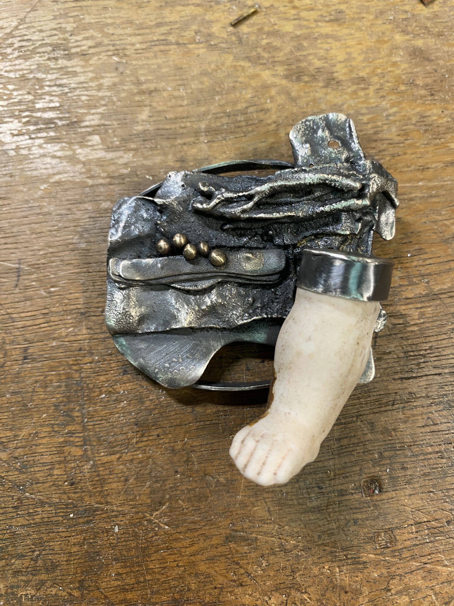 Multi-textured oval of Sterling silver with bronze bitlets and an antique doll's leg (or arm?) on one side