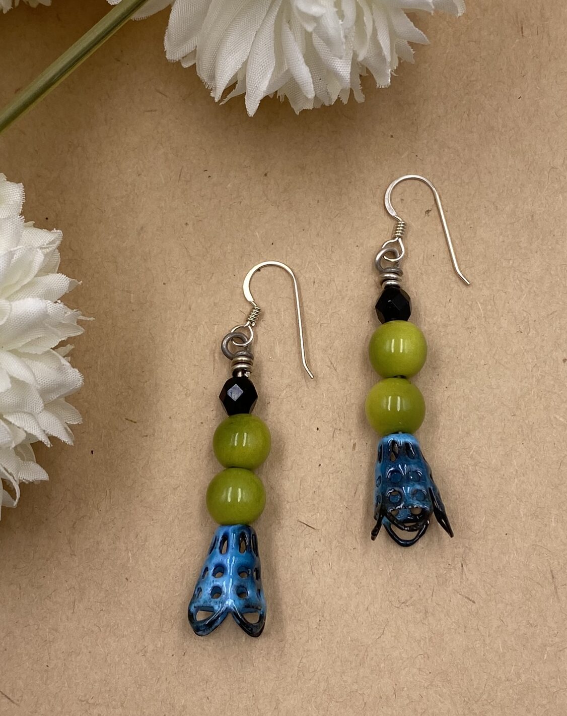 Earrings with black faceted glass bead at the top followed by two lime green tagua nut beads and a blue caged cone of enameled copper