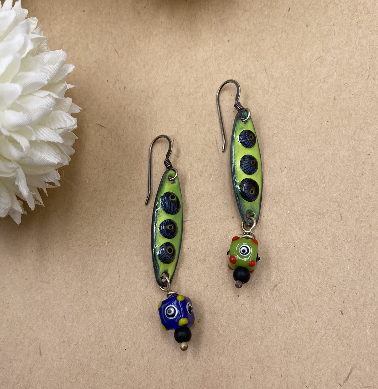 Brightly colored enameled copper peapod shaped drops in lime green with blue dots. Each earring has a different glass bead beneath - one blue with green and one green with red