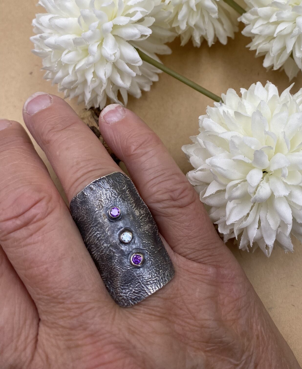 A curve of silver rectangle hugs your finger. Purple and white CZs adorn the crest of your finger.