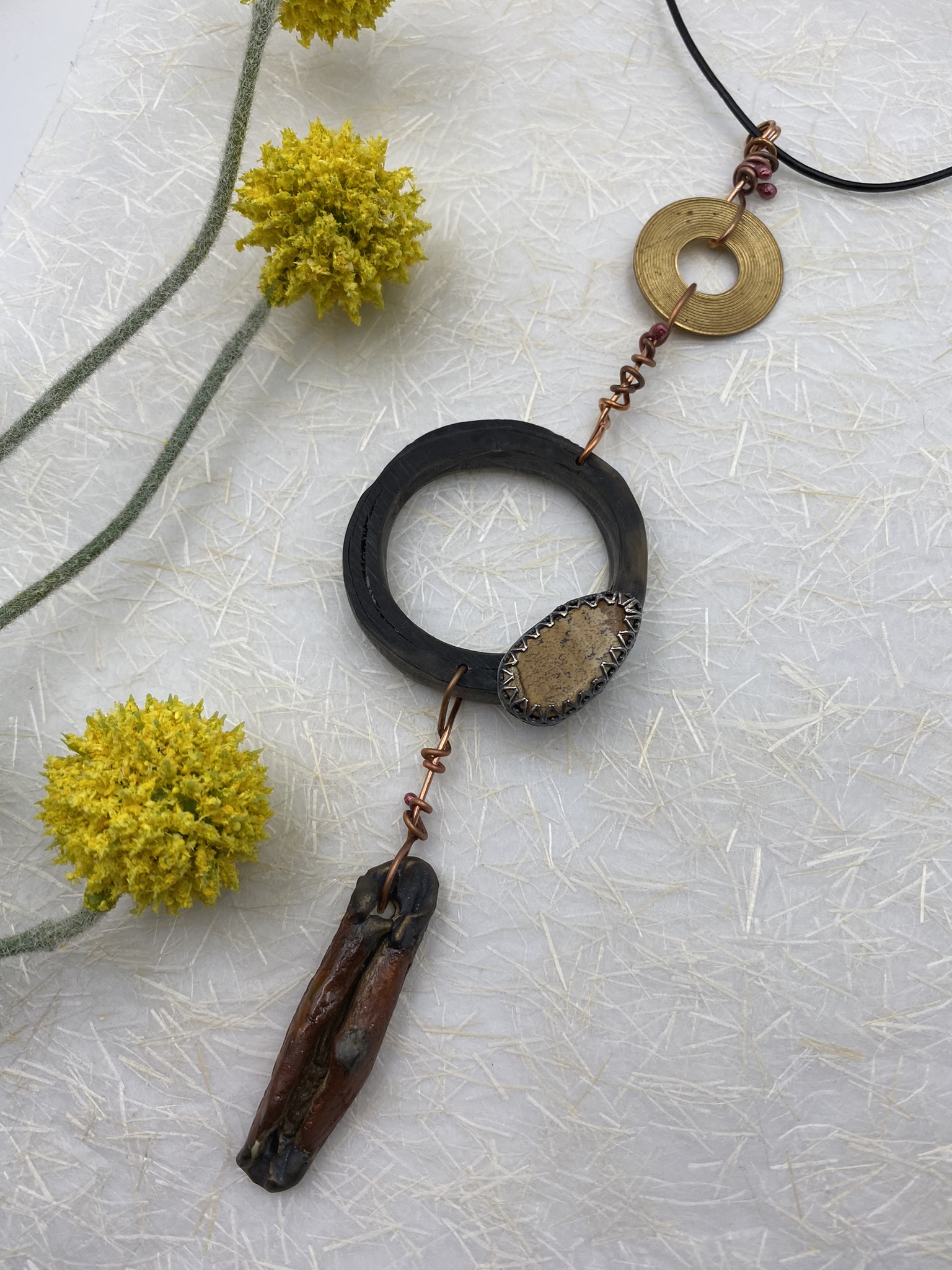 Buffalo horn supporting picture jasper, an orange, organic dangle, and a brass circle at the top suspended on a leather cord.