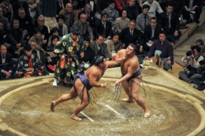 Two sumo wrestlers on the dohyo in Japan with a shinpan.